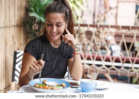 Eating out, lifestyle and travelling concept. Portrait of pretty european woman eating at restaurant table healthy food, drinking coffee, dining alone, smiling, tourist at cafe of her hotel Royalty-Free Stock Photo #1704131023
