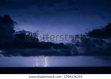 A distant thunderstorm over the sea with the silhouette of a ship on the horizon