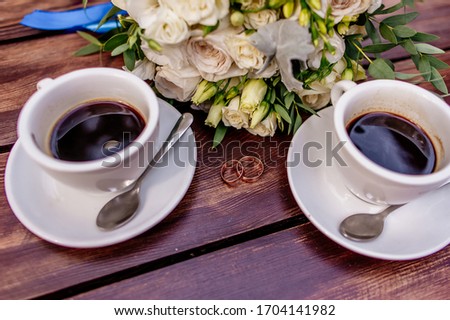 Two cups of coffee on the table, with wedding rings.