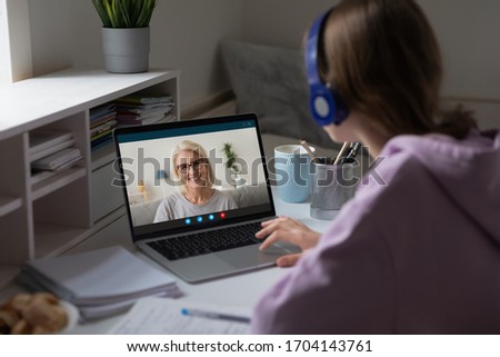 Distant lesson with middle-aged teacher. Adult grownup daughter or granddaughter talk with 60s grandmother use videocall, videoconference users, online meeting, over girl shoulder computer screen view Royalty-Free Stock Photo #1704143761