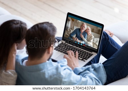 Couple communicating with elderly parents living abroad using computer and videocall application, laptop screen view over spouse shoulder. Distant virtual communication modern technology usage concept Royalty-Free Stock Photo #1704143764