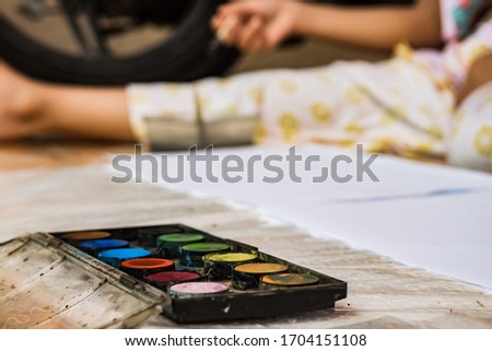 Watercolor palette with brightly colored paints and brush is being used by children to paint at home. Concept of children useful hobbies during stay at home or lockdown.