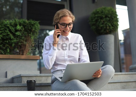 Happy entrepreneur working with a phone and laptop near the office. Royalty-Free Stock Photo #1704152503