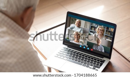 Older generation and modern technologies for virtual visual communication concept. Old man makes videocall talking with relatives or friends by video conference app, pc screen view over male shoulder Royalty-Free Stock Photo #1704188665