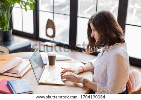 Business woman in white shirt working at laptop at home office, drinking coffee. Distance learning.Chat on mobile. Wooden table,organizer.Remote work place.Quarantine of coronovirus pandemic covid-19. Royalty-Free Stock Photo #1704190084
