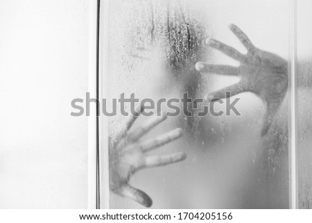 Hands touching frosted glass. Conceptual scream for help, depression, stress, panic. Human hand and unrecognizable silhouette behind wet glass in shower. Bathroom. Shadow. Hands concept. 
