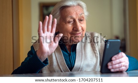 Authentic shot of a happy grandmother is making a selfie or video call to relatives with a smartphone at home. Concept of technology, modern generation,family, connection, authenticity Royalty-Free Stock Photo #1704207511