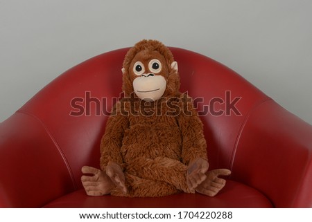 A stuffed animal in a Yoga pose sittning in a red armchair