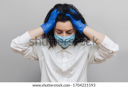 Young nurse doctor in a protective blue medical mask holds his head in his hands. Physical fatigue, moral exhaustion.The concept of quarantine, pandemic, control of the coronavirus COVID-19.