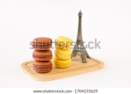 French lemon and chocolate macaroons on a wooden board. Near the Eiffel Tower figurine. Composition on a light background.