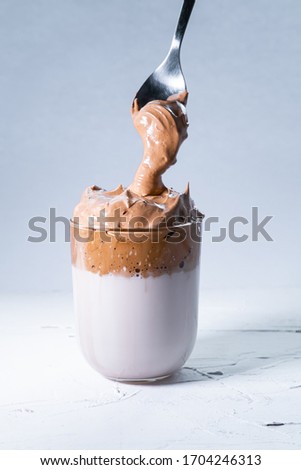 Korean dalgona coffee and spoon with creamed coffee falling into a glass on white background. Vertical picture.