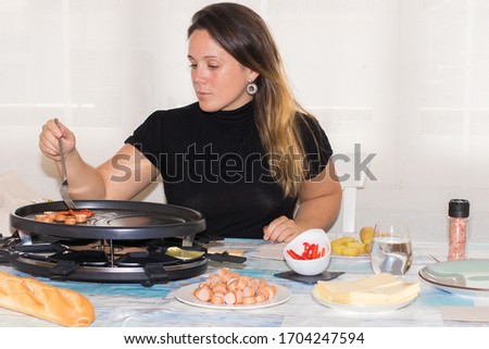 Girl cooking raclette at home waiting for his friend.