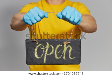 Quarantine end. Courier in yellow uniform, protective mask and gloves Holding a sign with the text Open. Delivery service 