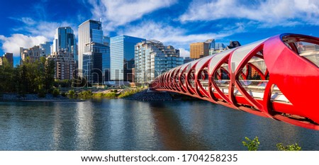Peace Bridge across Bow River with Modern City Buildings in Background during a vibrant summer sunrise. Taken in Calgary, Alberta, Canada. Royalty-Free Stock Photo #1704258235
