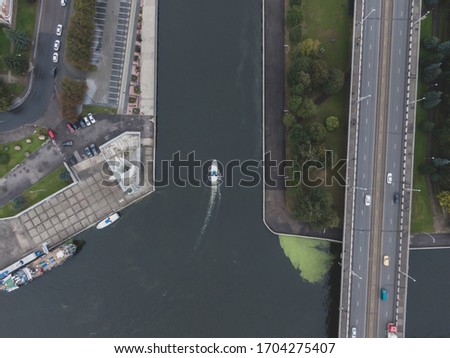 Aerial drone photo of a small motorboat flowing through the Kaliningrad canal. Verical drone view.
Main city road on right side.