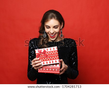 Portrait of beautiful woman in evening dress holding opened present box isolated over red