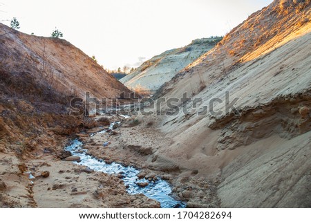 A small river flowing between two mountains. The creek from which the river begins. Sand and stone mountains.