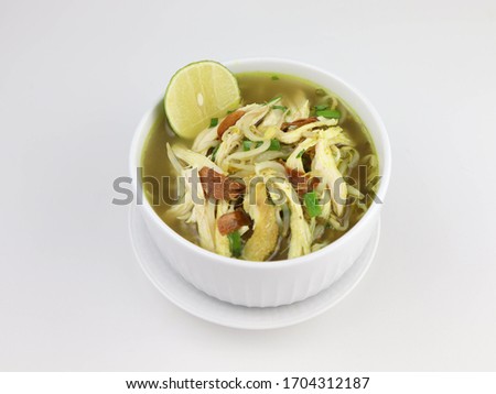 Soto Kudus ayam is a traditional Indonesian chicken soup from Kudus, Central Java. Mainly composed of broth, chicken and vegetables, served in white bowl on the wooden table. White isolated.