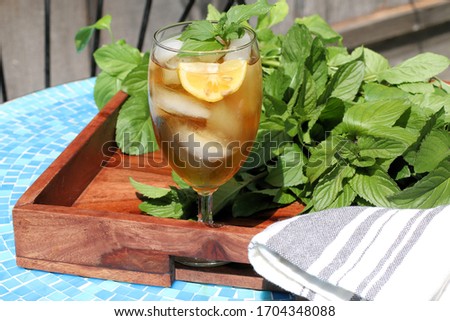 Glass of Iced Tea on a wooden tray sitting on a  blue patio table, fresh mint garnish