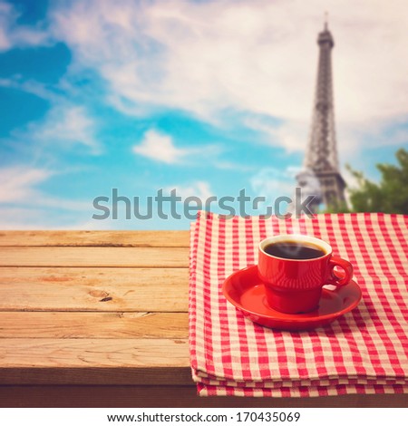 Coffee cup with checked tablecloth on wooden table over Eiffel tower in Paris, France