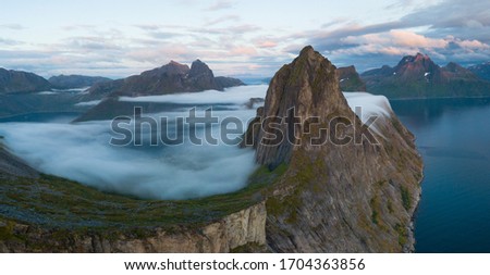 Panorama of Segla mountain, Senja, Norway. Magical fog at the base. Aerial photography of Lofoten Islands and Senja. Dramatic landscape during sunset. Hesten and Segla mountain. Royalty-Free Stock Photo #1704363856