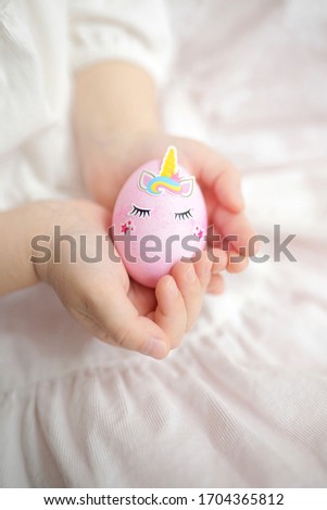 Little girl in the white dress holding pink unicorn egg. Easter holiday. Easter egg in the hands. Easter picture. Egg decoration.