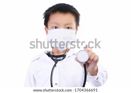 education and occupation concept. A cute asian boy wearing a self-protect mask and medical uniform holding stethoscope and looking at camera isolated on white. (Selective focus at stethoscope)