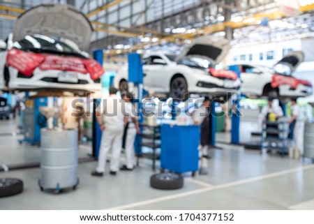 The picture is blurry while the mechanic works in the car service center. There are cars. Many customers come to use the oil change service.