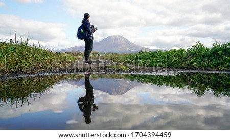 Reflection in water Woman holding medium format camera and looking view Mountain landscape among cloudy in blue sky 