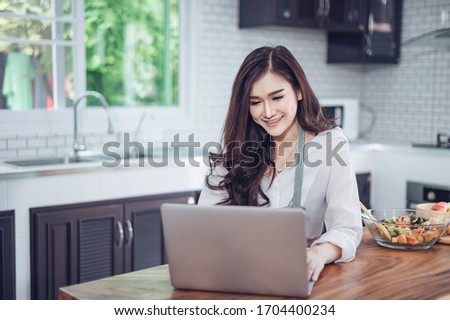 Image of young pretty woman standing in kitchen using computer laptop and cooking with the tomatoes and avocado, Cooking from home, Photo with noise and grains