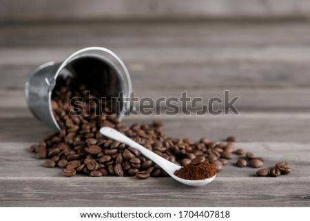 Arabica coffee beans in a small miniature bucket. ground coffee in a white ceramic spoon on a wooden background.