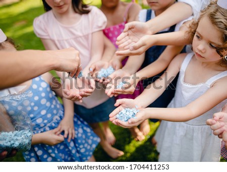 Unrecognizable small children outdoors in garden in summer, holding confetti.