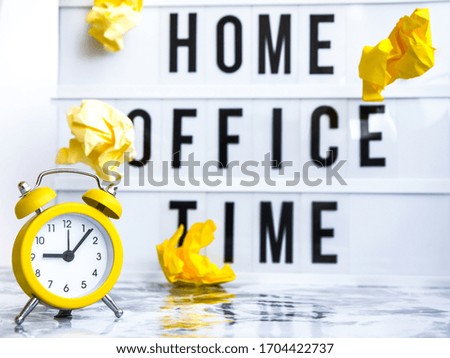 lightbox with text HOME OFFICE TIME in front concrete background with alarm clock, copy space, banner for freelance coronavirus covid-19 quarantine crumpled yellow papers, business planning and