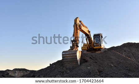 Yellow excavator during earthmoving at open pit on blue sky background. Construction machinery and earth-moving heavy equipment for excavation, loading, lifting and hauling of cargo on job sites Royalty-Free Stock Photo #1704423664