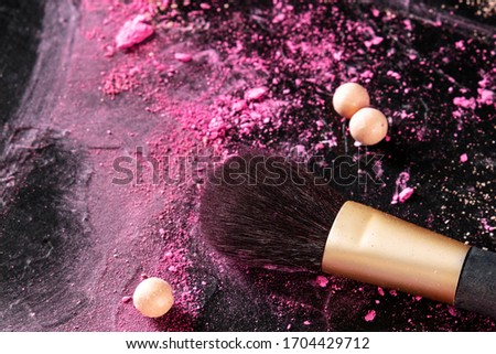 A make up brush with crushed cosmetics and pearls on a black background with copyspace