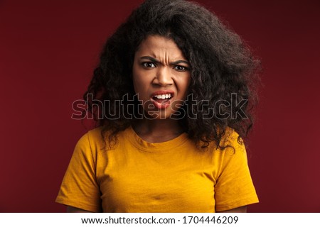 Image of disappointed brunette african american woman with curly hair frowning and expressing outrage isolated over red background Royalty-Free Stock Photo #1704446209