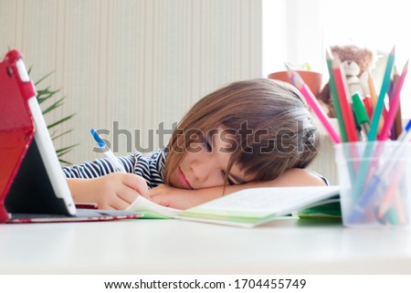 girl schoolgirl child 8 years old is engaged in distance learning does lessons on a tablet writes in a notebook Royalty-Free Stock Photo #1704455749