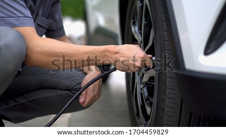 man filling air in the tires of his car (inflating tire) Royalty-Free Stock Photo #1704459829
