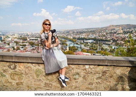 Attractive beautiful young girl holding modern mirror camera in the city. Female traveller and old house background