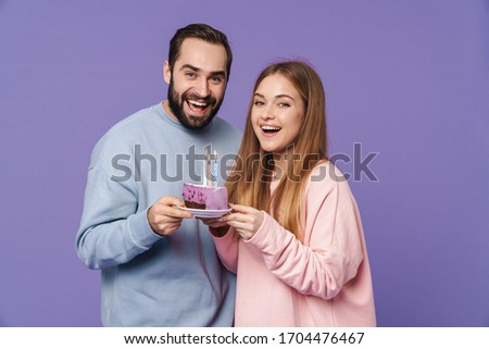 Image of a emotional happy young loving couple isolated over purple wall background with birthday cake.