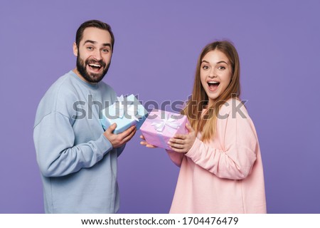 Image of excited positive young loving couple isolated over purple wall background give a gifts for each other.