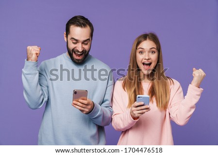 Picture of excited surprised loving couple isolated over purple background using mobile phones make winner gesture.