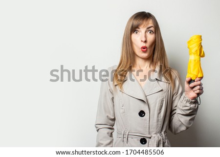 Portrait A young friendly woman in a classic jacket with a surprised face holds a yellow umbrella on an isolated light background. Emotional face. Bad weather, rain, weather forecast