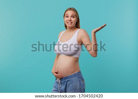 Displeased young pretty white-headed pregnant woman dressed in casual wear raising confusedly palm while looking at camera, standing over blue background