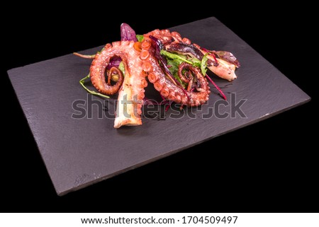 Octopus tentacles with arugula on a black stone square plate. High resolution, black background.
