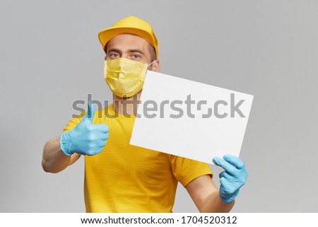 Courier in yellow uniform, protective mask and gloves delivers takeaway food and coffee. Delivery service under quarantine. Holding a white sign for text