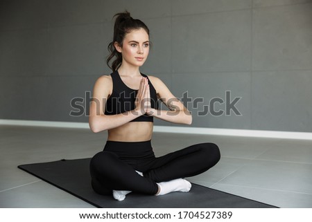 Photo of focused young woman in sportswear meditating and holding palms together while sitting on mat