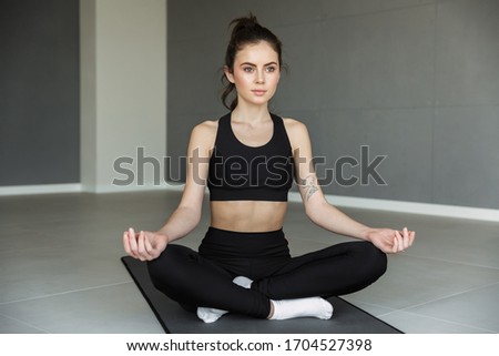 Photo of focused young woman in sportswear meditating while sitting with legs crossed on mat