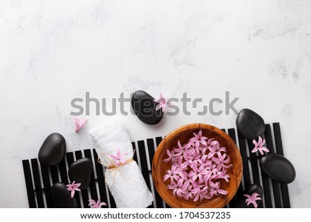 Beauty, spa background with massage stone and flowers in bowl on white table from above. Relaxation and wellness concept. Flat lay.