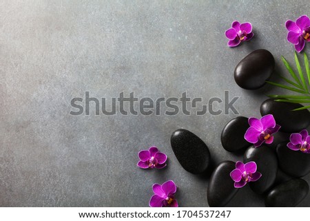 Spa composition with flowers, green leaves and massage stone on gray background top view. Beauty treatment and relaxation concept. Flat lay. 
